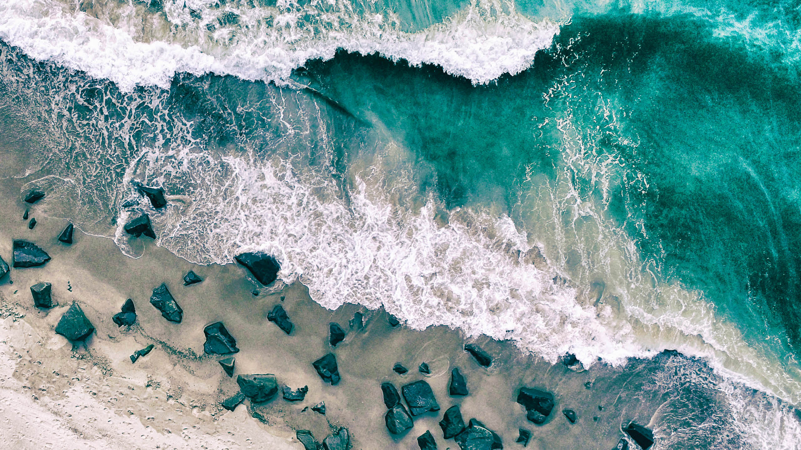 The sea with waves and ripples and the shore with rocks. This image was photographed from above with a drone.