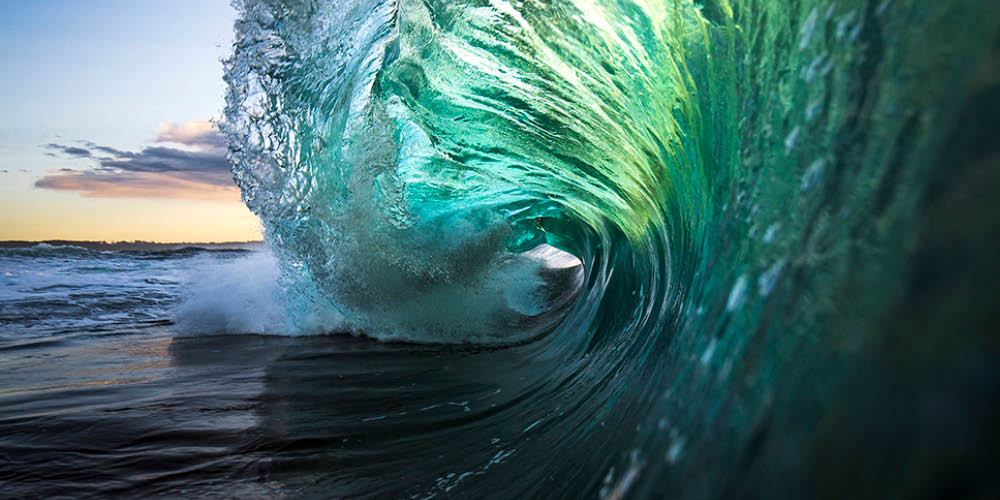 Large colourful wave breaking in ocean over reef and rock